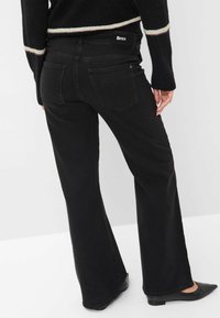 Jeans neri svasati con una texture liscia e due tasche posteriori. Presentano una vita con marchio e sono abbinati a scarpe nere.