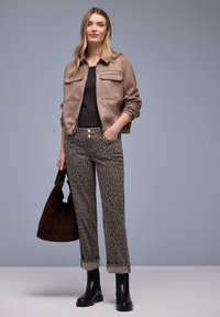 Ruskea mokkatakki, jossa kaksi etutaskua, musta toppi, teksturoidut harmaat leopardi-kuvioiset housut, ruskea laukku ja mustat nilkkurit.