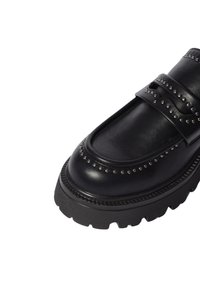 Mocassino in pelle nera con borchie metalliche e una suola spessa e testurizzata. Presenta una tomaia liscia, punta arrotondata e fasce decorative.