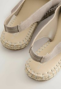 Sandales espadrilles en cuir beige avec brides de cheville en daim et semelles en jute cousues sur un fond clair.