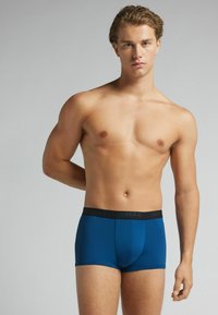 Calzoncillos bóxer azules con una cinturilla elástica negra que presenta una marca. El material parece suave, con un diseño ajustado que acentúa la forma del cuerpo.