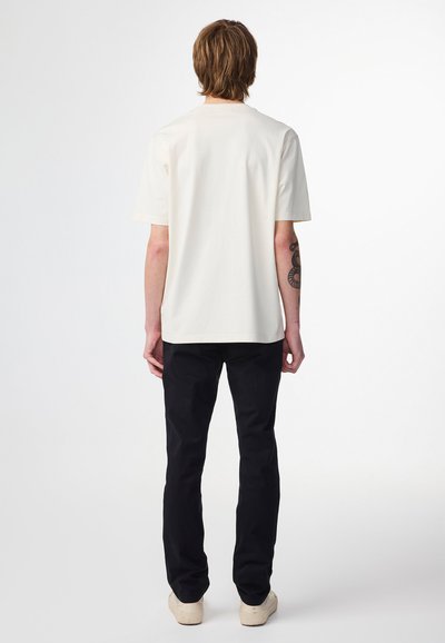 Off-white bomulds t-shirt med korte ærmer, ensfarvet design, afslappet pasform; båret med sorte bukser og lyse sko.