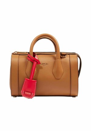 Sac à main en cuir fauve avec double poignées et une étiquette en cuir rouge attachée, portant le nom de la marque Lancel à la fois sur le sac et l'étiquette.