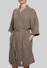 Lengvas rudas chalatas su raukšlėta tekstūra, su diržu liemenyje, plačiomis rankovėmis ir šoninėmis kišenėmis. Sukurtas su šaliko tipo apykakle.