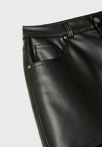 Zwarte leren rok met een gladde textuur, een zijzak met zichtbare stiksels en metalen knoopaccenten aan de taille.