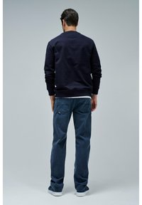 Sudadera de un oscuro azul marino con puños y dobladillo de canalé, combinada con jeans azules que presentan una sutil textura y bolsillos traseros. Calzado casual completa el conjunto.