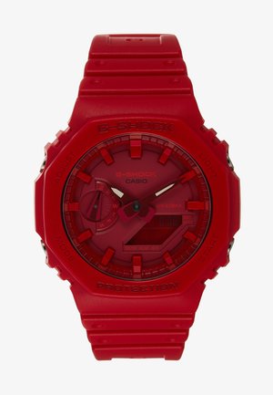 Reloj G-Shock rojo con una pantalla digital y analógica, correa de goma y caja hexagonal. Presenta marcadores de hora audaces y botones. Resistente al agua.