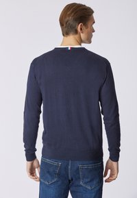 Maglione lavorato a maglia blu navy con maniche lunghe e scollatura a girocollo. Orlo e polsini a coste. Piccolo dettaglio rosso, bianco e blu sul collo.