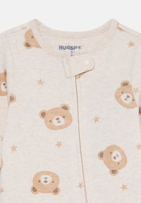 Helles beige Babykleid mit weicher Textur und Bären- und Sternmustern. Mit einem Druckknopf am Hals zum einfachen Ankleiden.