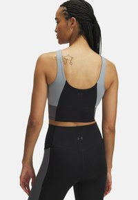 Vrouw met gevlochten haar, gekleed in een twee-kleurige sportbeha en zwarte leggings, met een kleine wereldkaart tatoeage op haar bovenrug.