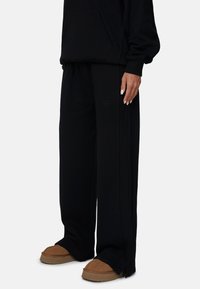 Zwarte oversized hoodie met een voorzak, gecombineerd met wijde zwarte broek. Opvallende ribbelstructuur en subtiele branding op de broek.