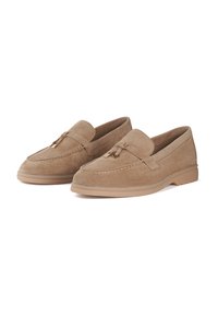 Mocassins en daim beige clair avec un bout rond, des coutures décoratives et un petit accent doré sur le dessus. La semelle en caoutchouc offre une bonne adhérence.