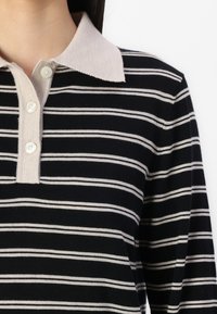 Polo a maniche lunghe a righe bianche e nere con colletto beige chiaro e chiusura frontale a tre bottoni, texture in maglia.