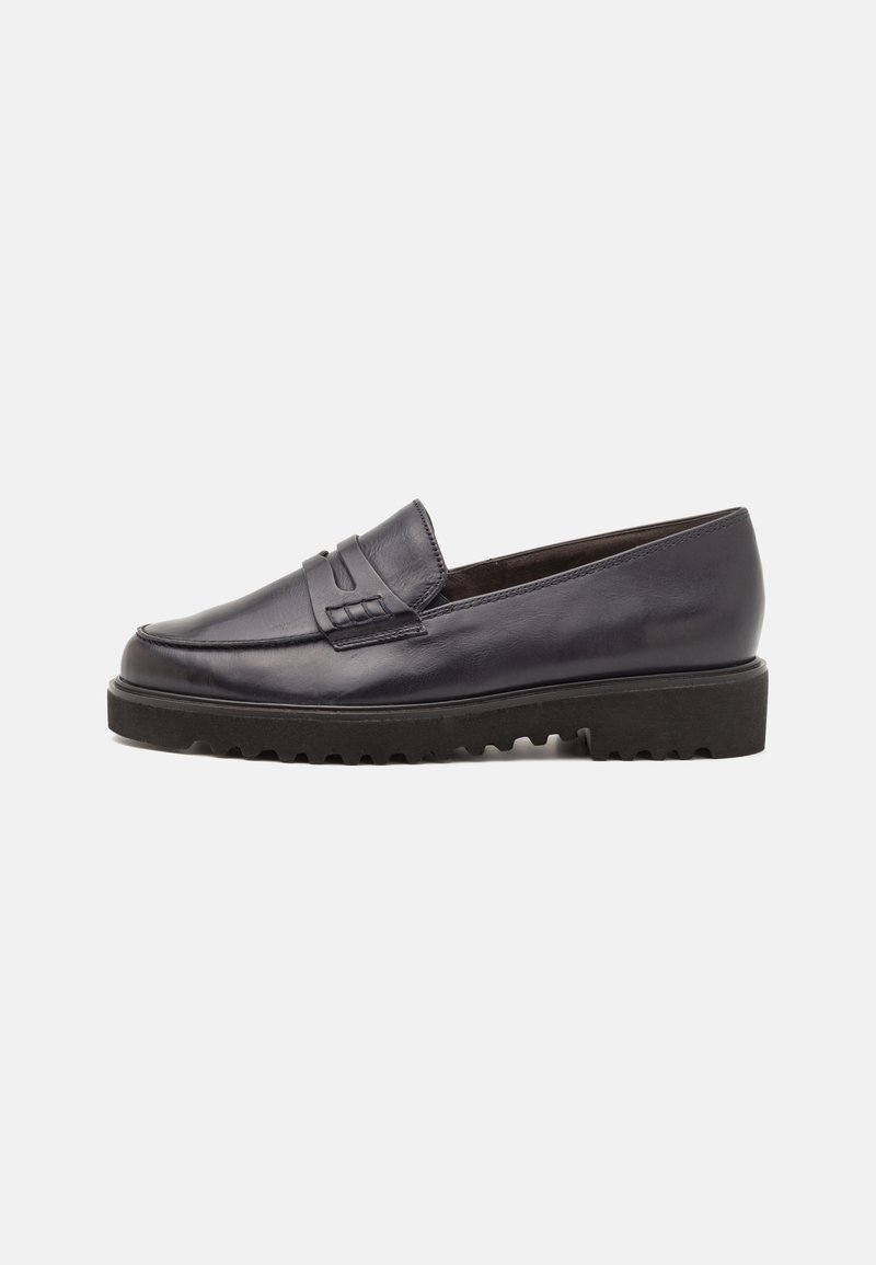 Mocassin en cuir noir avec semelle épaisse à rainures et détail de bride décorative sur le dessus, présenté sur fond blanc.