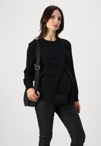 Svart stickad tröja med rund halsringning och ribbade ärmslut, kombinerat med svarta glänsande leggings i leopardmönster och en liten axelväska.