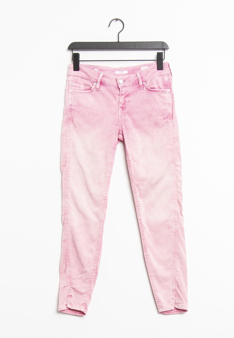Jeans skinny de denim rosa con un acabado desgastado, que cuentan con dos bolsillos delanteros, bolsillos traseros y una cremallera. Colgados en una percha negra.