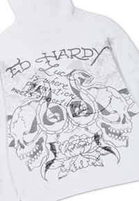 White hoodie with black graphic of two snakes coiled around skulls, flowers, and text reading "Ed Hardy" and a motivational phrase.