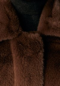 Hnědá umělá kožešina s měkkou, hustou texturou; detail límce, doplněný o černý pletený oděv pod ním.
