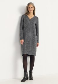 Grå stickad klänning med V-ringning, långa ärmar och en lätt nedhasad kant. Matchas med svarta ankelboots och strumpbyxor.