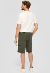 Olivgrüne Cargoshorts mit aufgesetzten Taschen und einem schwarzen Label, kombiniert mit einem weißen T-Shirt mit kurzen Ärmeln. Aus Baumwolle, lockere Passform.