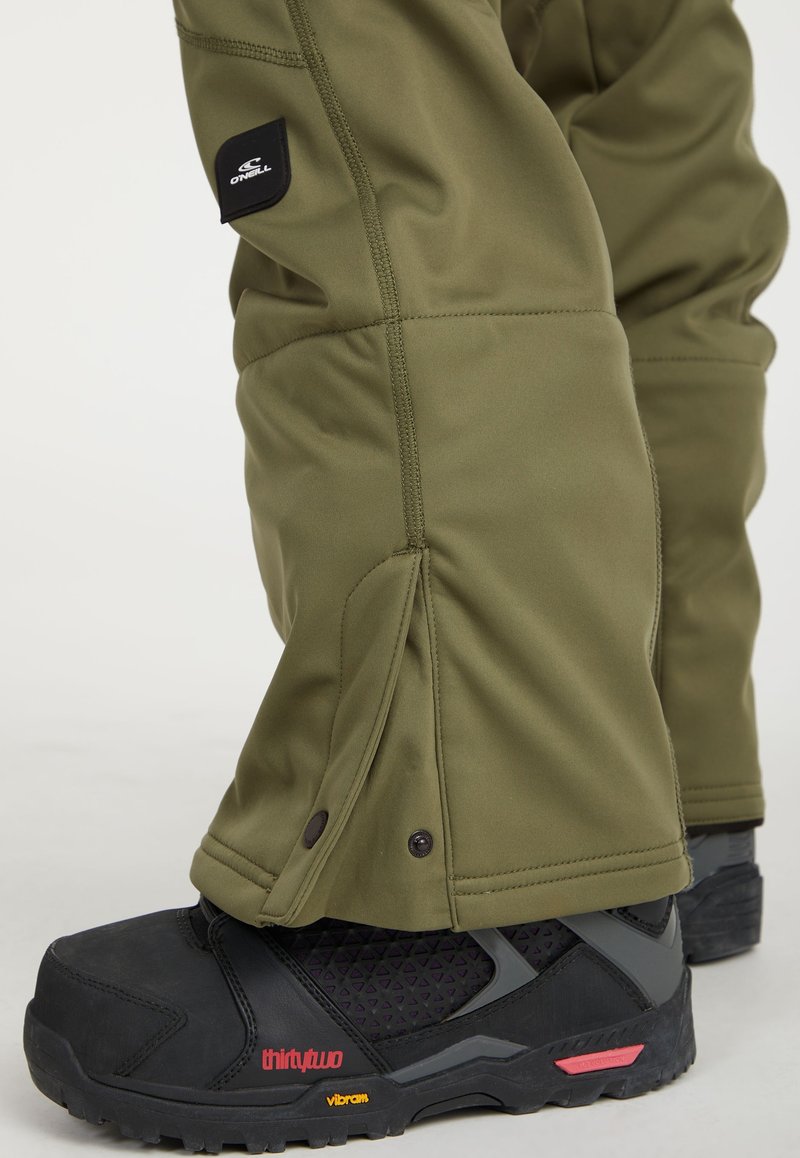 Olivgrüne Schneehose mit glatter Textur, ausgestattet mit Reißverschluss und einem Logo-Aufnäher. Schwarze Wanderstiefel mit gemustertem Innenfutter.