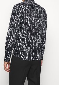 Camicia a maniche lunghe realizzata in tessuto leggero, caratterizzata da un motivo frastagliato monocromatico in bianco e nero con colletto classico.