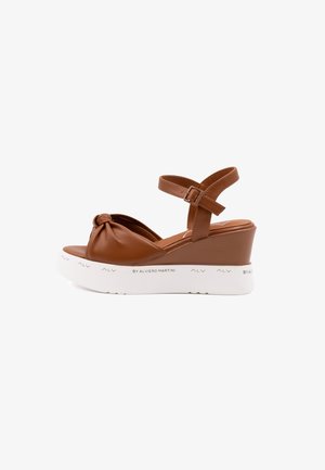 Brown leather wedge sandals with a knotted strap design, adjustable ankle strap, and a white platform sole featuring subtle branding.