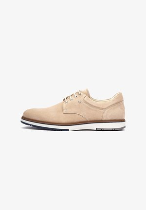 Chaussure de ville à lacets pour homme en daim beige avec semelle blanche et marine, petit talon, et coutures apparentes, présentée de profil sur fond blanc.