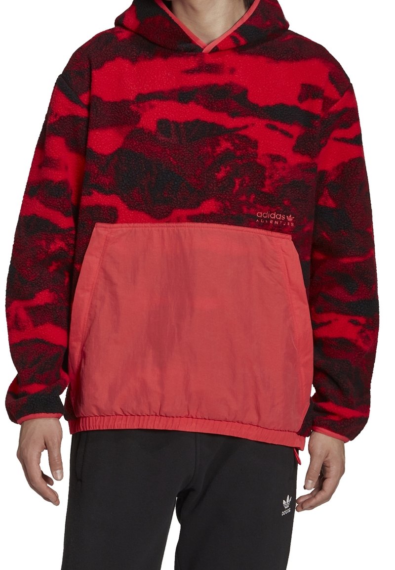 Röd och svart fleece-hoodie med känguruficka, med texturerad tyg och en slät röd panel i botten. Adidas-logga fram.