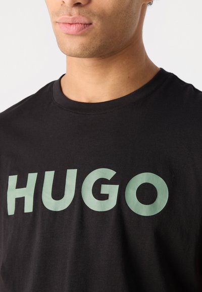 Черна памучна тениска с голямо ментово-зелено лого "HUGO" отпред. Кръгло деколте и къси ръкави.