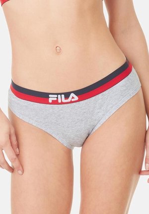 Femme portant des sous-vêtements FILA gris avec une ceinture rouge et noire, montrant le ventre et une partie des mains sur un fond blanc.