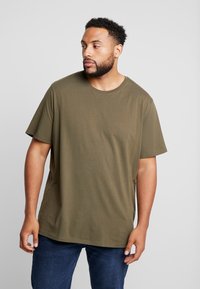 Olijfgroene t-shirt met korte mouwen, gemaakt van zachte stof. Heeft een ontspannen pasvorm en een ronde hals. G gecombineerd met blauwe jeans.