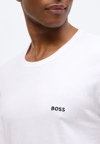 White cotton T-shirt featuring a round neckline and embroidered "BOSS" logo in black on the left side of the chest. Smooth texture.