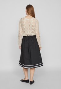 Krämsfärgad, virkade långärmad topp med öppet mönster; i kombination med en svart, knä-lång kjol med vit zigzagkant. Platta svarta skor.