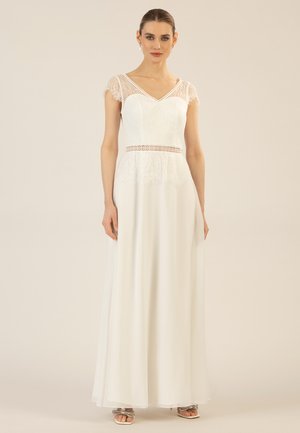 Das weiße Spitzen- und Chiffonkleid hat ein tailliertes Oberteil mit V-Ausschnitt, kurzen Spitzensäumen und einem bestickten Taillenbund, der bis zum Boden fließt.