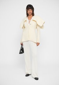 Blazer branco texturizado com gola oversized, fecho de botão, combinado com calças largas de malha e uma pequena mala preta. Calçado preto.