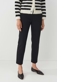 Zwarte slim-fit broek van een gladde stof, met een middelhoge taille en een cropped lengte, gecombineerd met puntige zwarte ballerina's en een gestreepte cardigan.