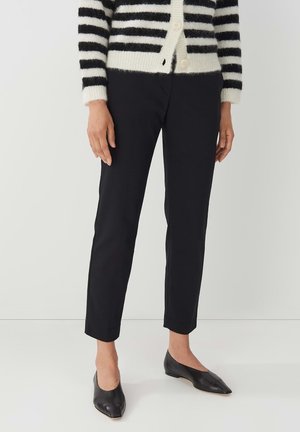 Black slim-fit trousers with a smooth texture, featuring a mid-rise waist and cropped length, paired with pointed black flats and a striped cardigan.