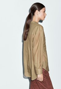 Lange mouwen, olijfgroen shirt met een relaxte pasvorm. Voorzien van een knoopsluiting aan de voorkant, een gebogen zoom en doorzichtige stofdetails.