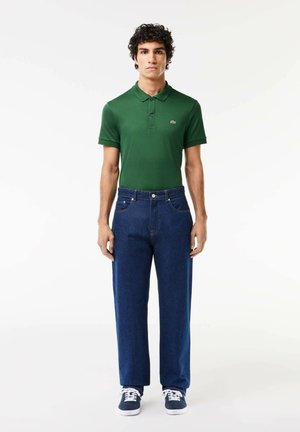 Groene katoenen polo met korte mouwen, gecombineerd met een blauwe rechte jeans. Sneakers in marineblauw en wit maken de outfit af.