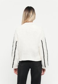 Gehaakte trui in het wit met zwarte decoratieve stiksels langs de mouwen. Heeft een ontspannen pasvorm en een cropped ontwerp.