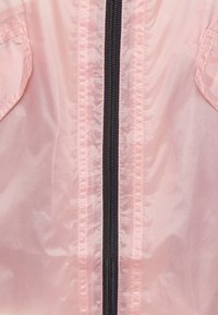 Jasnoróżowa kurtka przeciwwiatrowa z czarnym zamkiem błyskawicznym na całej długości, kieszeniami na piersi oraz gładką, błyszczącą teksturą.