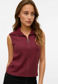 Bourgogne ärmlös topp med ribbad krage, dragkedja fram och en figurnära design. Slät textur och cropped längd.