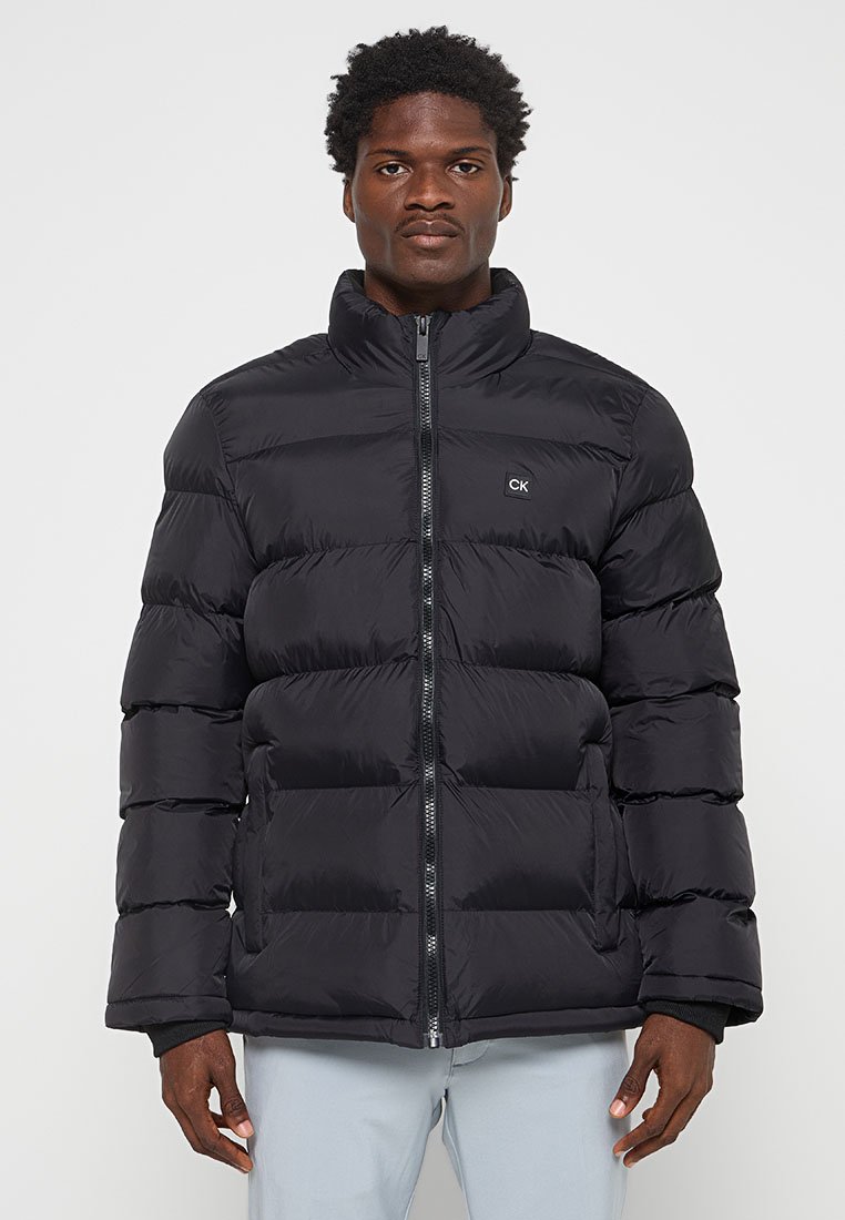 Schwarze Daunenjacke, gestepptes Design, hoher Kragen, Frontreißverschluss, Logo auf der linken Brust. Glattes, glänzendes Material mit ausreichend Isolation.