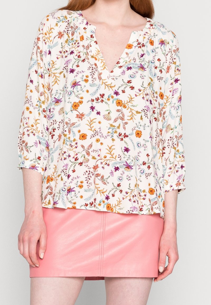 Weiße Bluse mit buntem Blumenmuster, mit einem V-Ausschnitt und Dreiviertelärmeln, kombiniert mit einem rosa Leder-Minirock.