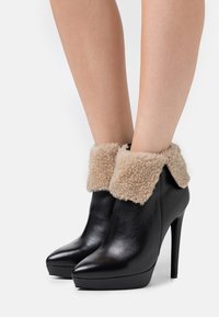Stivali neri in pelle con un bordo in pelliccia sintetica beige, punta affusolata e tacco a stiletto alto. Texture liscia con suola a piattaforma.