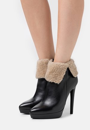 Mustat nahka nilkkurit, joissa on beige tekoturkiskaulus, terävä kärki ja korkea stiletto-korko. Sileä pinta ja alustakenkä.