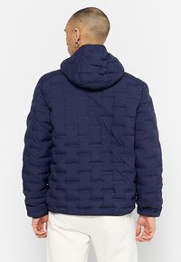 Granatowa kurtka puchowa o teksturowanym, pikowanym wzorze z kapturem. Wykonana z pozornie lekkiego materiału, z elastycznymi mankietami.