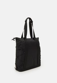 Bolsa tote negra de nailon con correas ajustables, que presenta una superficie texturizada y un detalle de bungee lateral para mayor funcionalidad. Cierre con cremallera.