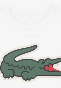 Λευκό βαμβακερό T-shirt με μεγάλο πράσινο γραφικό κροκόδειλου με κόκκινες λεπτομέρειες και μαύρο περίγραμμα. Στρογγυλή λαιμόκοψη, κοντά μανίκια.